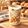 Digital concept of a ceramic travel mug with a croissant, baguette and wheat sprigs on a wooden bakery table.